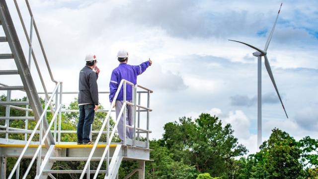 Men inspecting a wind turbine in the distance.
