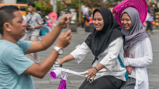 A man taking photos as tourists ride the bicycle in a tourist town in Jakarta.